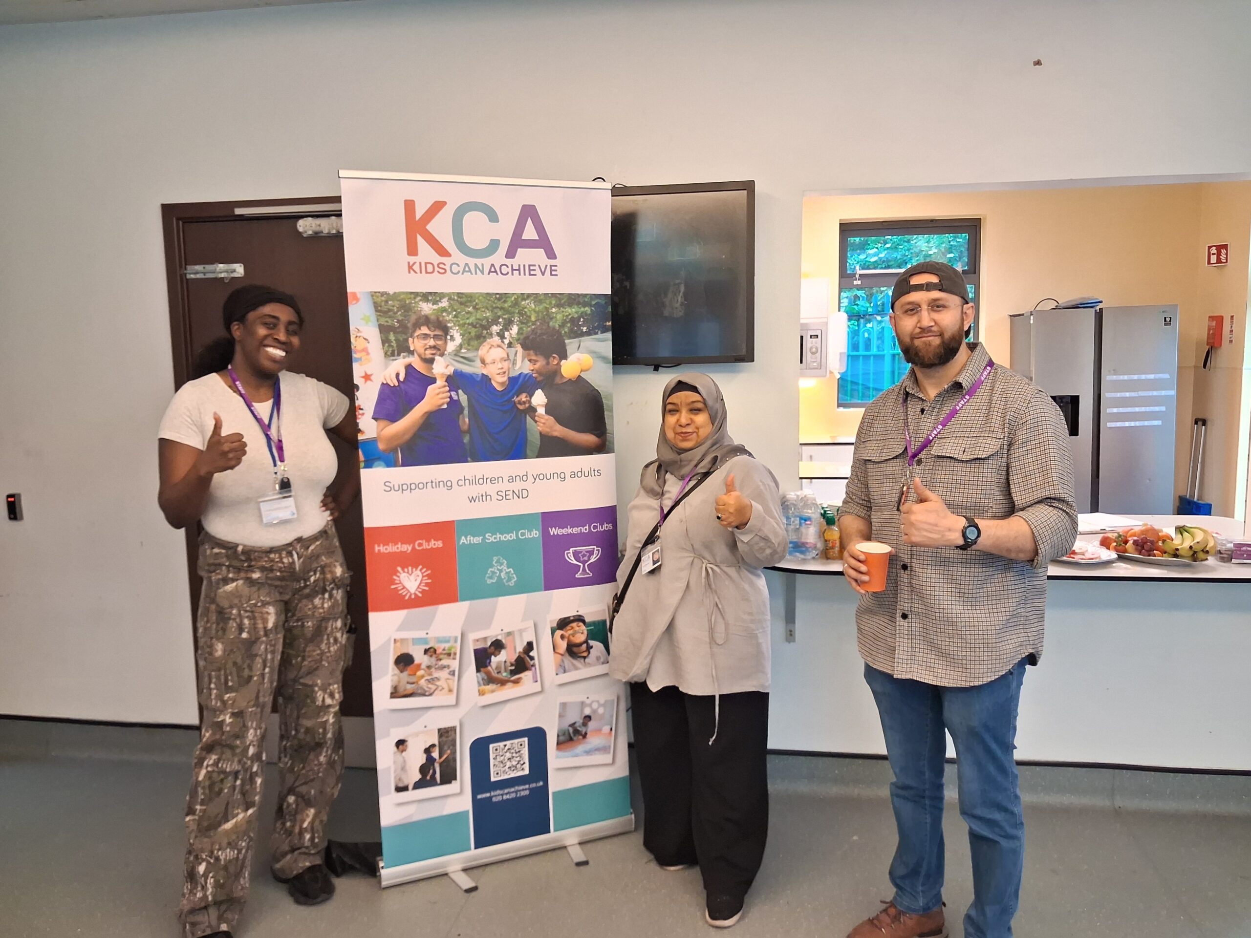 Group of staff next to a KCA pull up banner holding their thumbs up